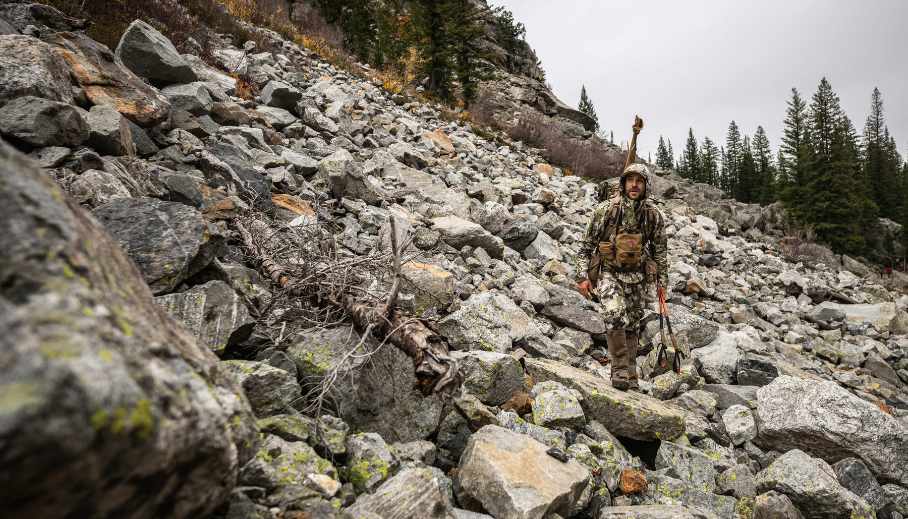 man in hunting camo hiking through rocky terrain